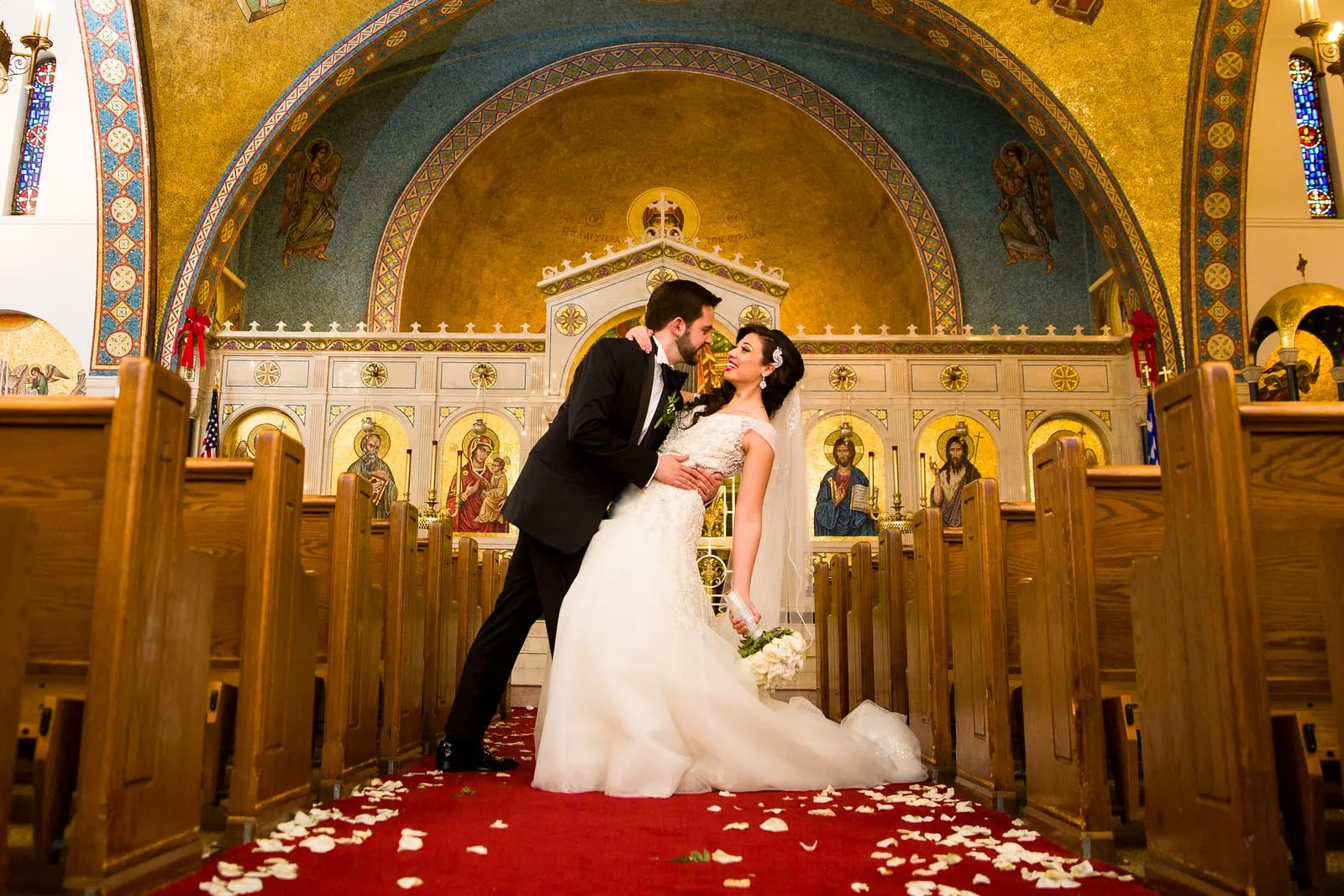 Groom dipping the bride for a kiss in the cathedral aisle under the golden dome