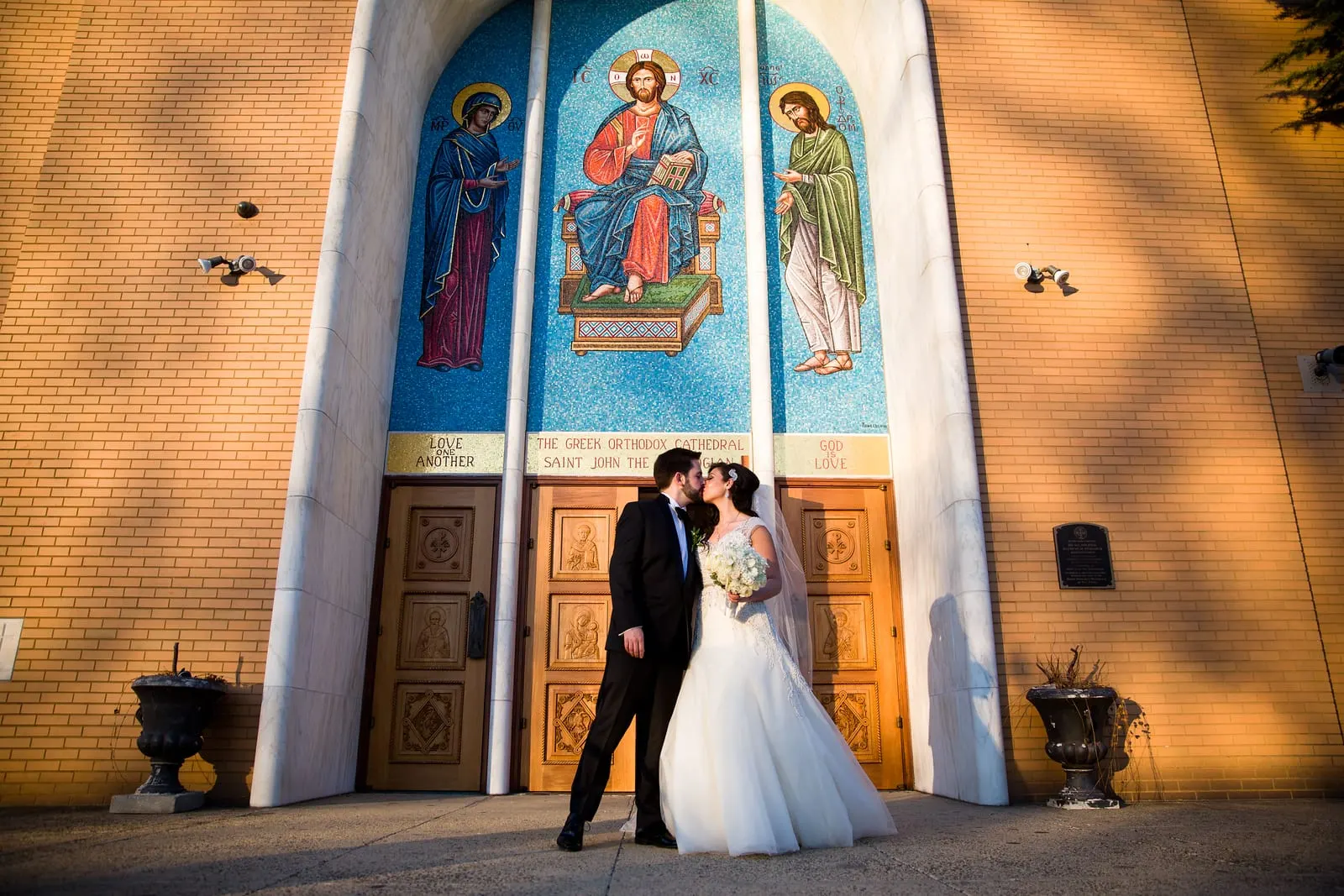 Bride and groom kissing at the cathedral doors beneath a mosaic of Christ