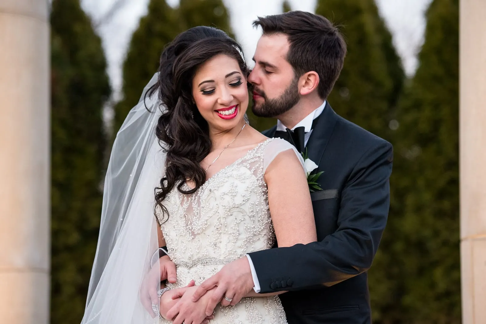 Groom holding the bride from behind as she smiles at the camera