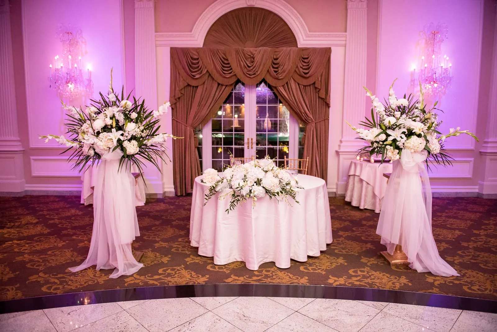 Sweetheart table framed by white flowers and draped curtains