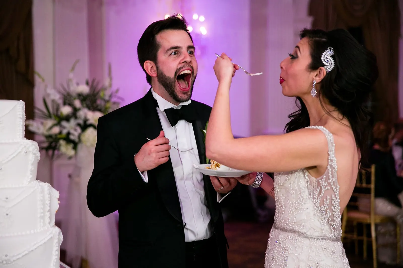 Groom laughing as the bride feeds him cake