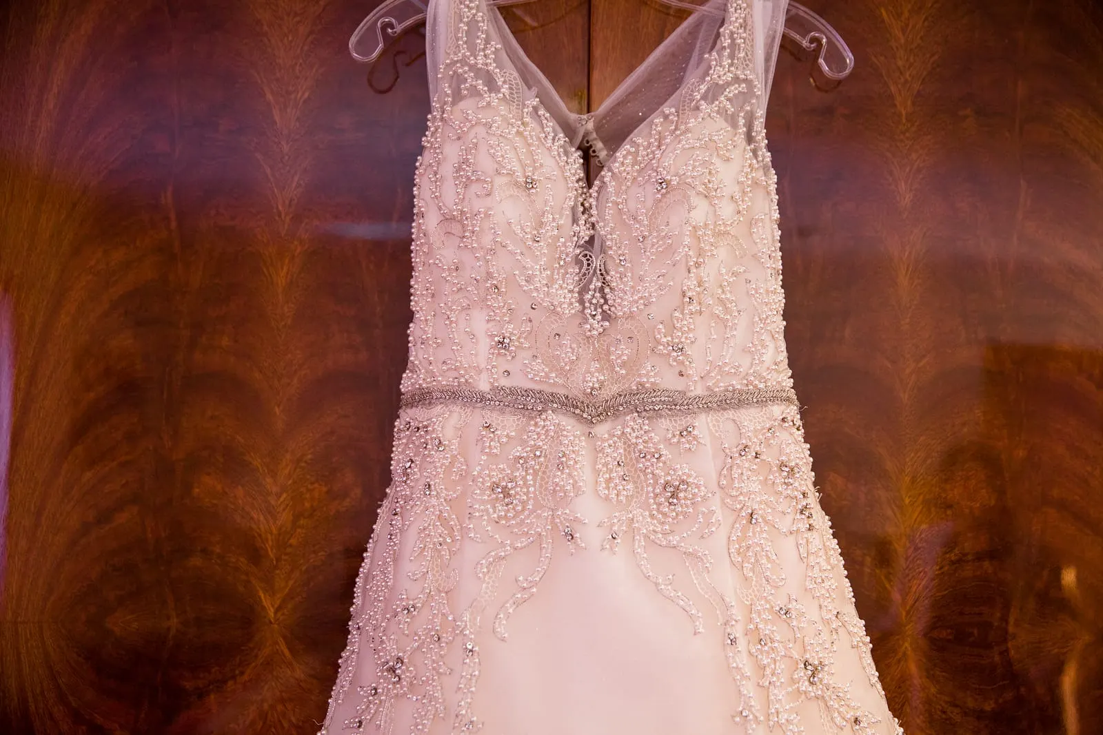 Beaded bodice of the wedding gown hanging against a wood-paneled wall
