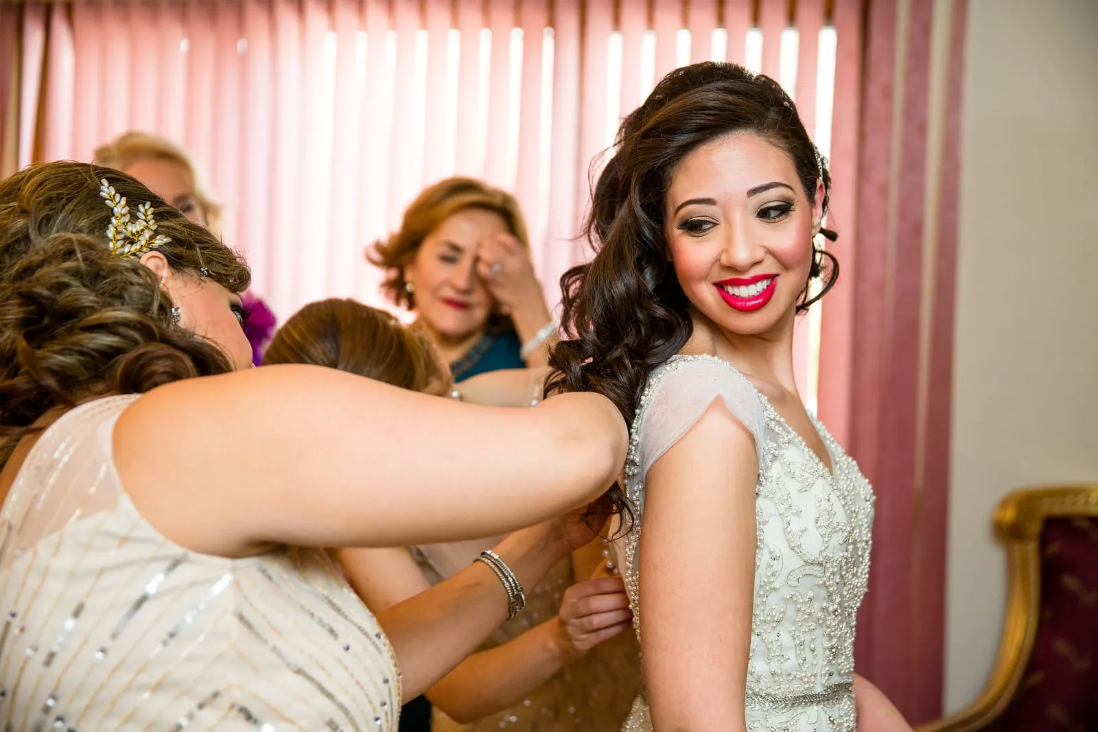 Bride laughing as her bridesmaids button her gown