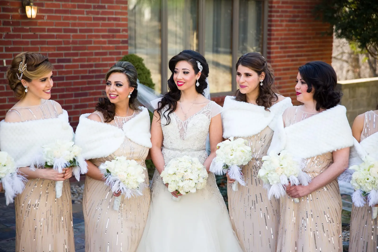 Bride with her bridesmaids in white fur wraps outside the house
