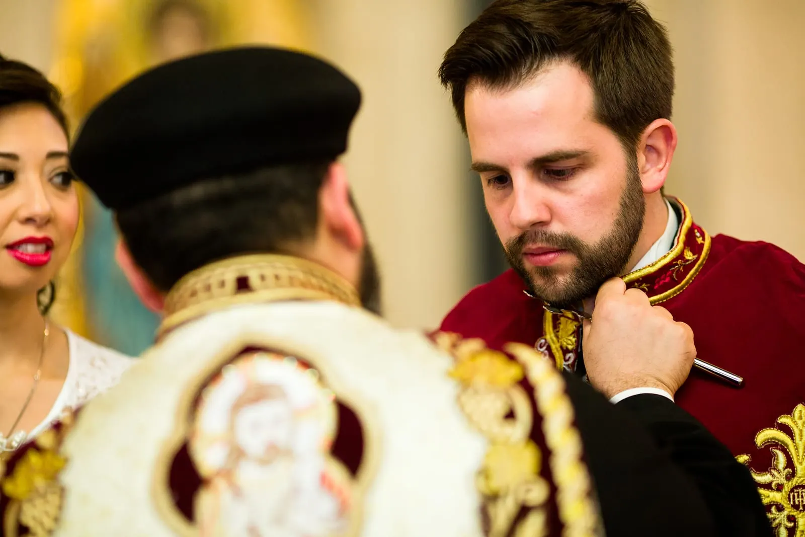 Priest robing the groom in a red and gold embroidered cape