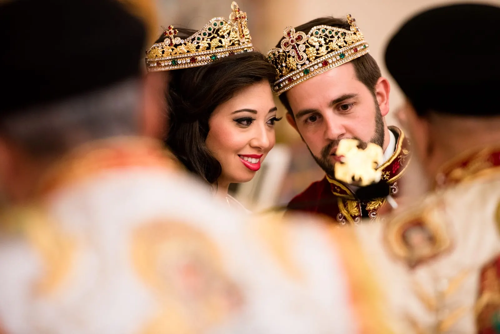 Crowned bride and groom framed by the priests' vestments