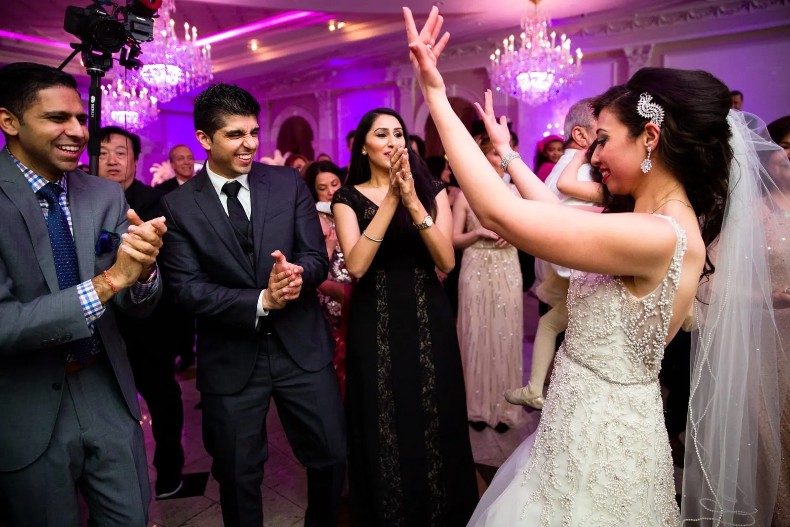 Bride raising her arms on the crowded dance floor