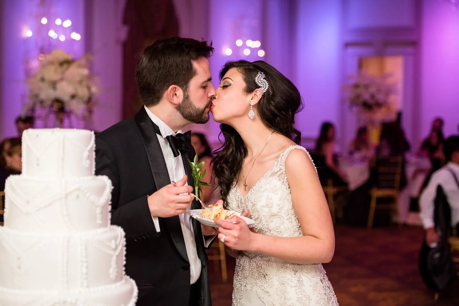 Bride and groom kissing beside the white wedding cake