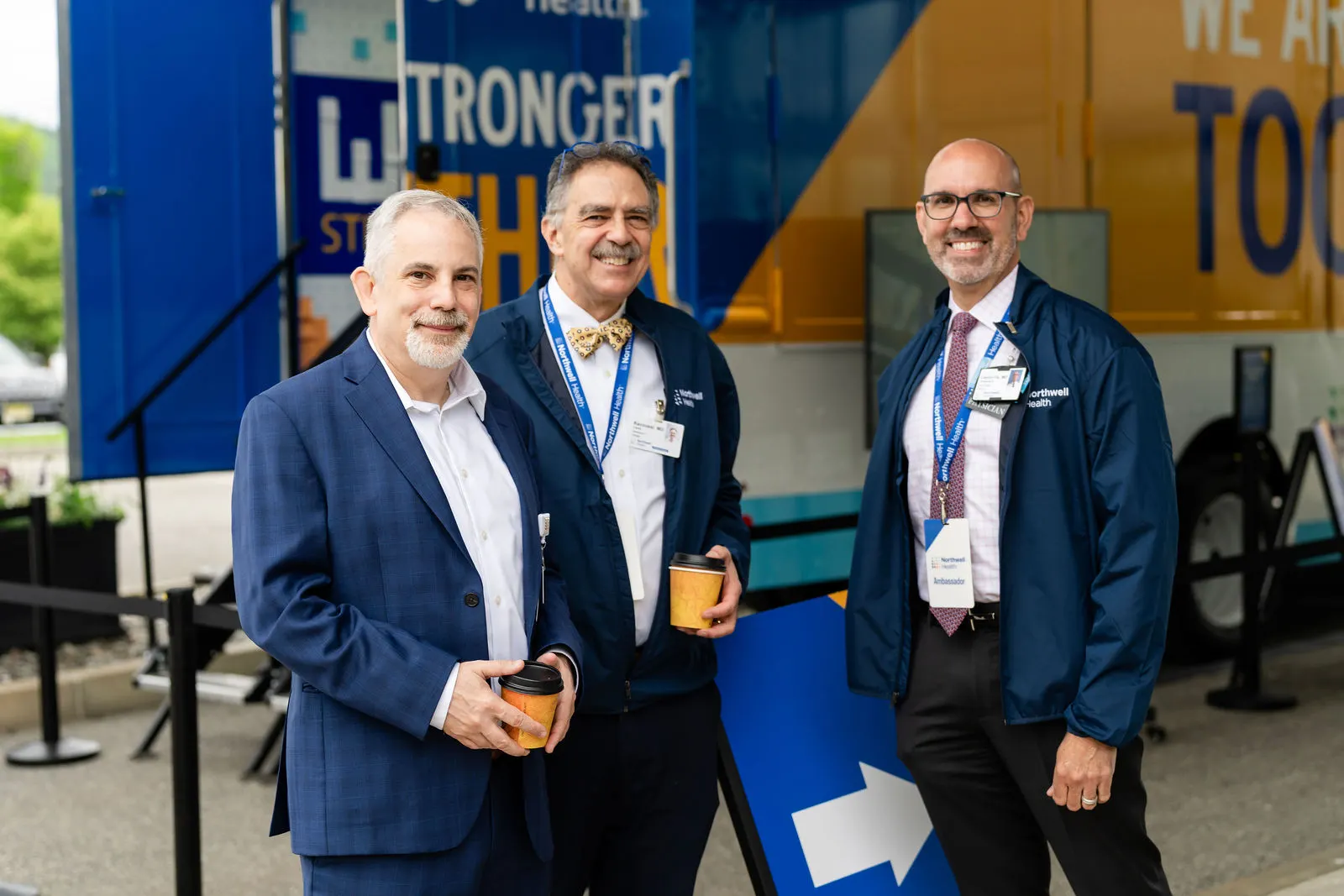 Three leaders smiling beside the We Are Stronger Together truck at Sharon Hospital