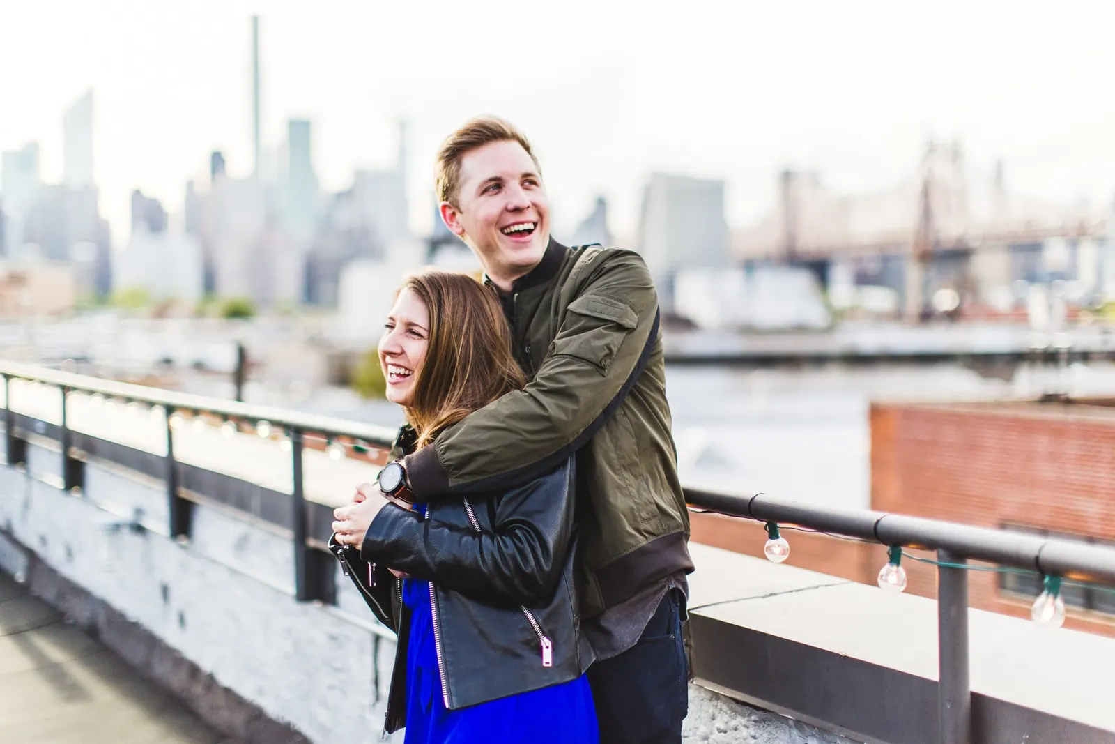 Laughing couple embracing along the waterfront with the Manhattan skyline in the distance