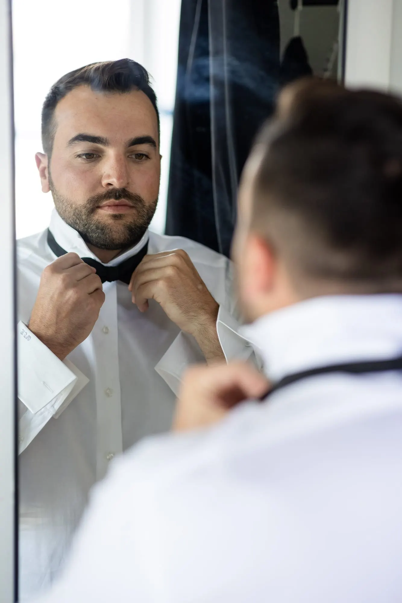 Groom adjusting his bow tie in the mirror while getting ready