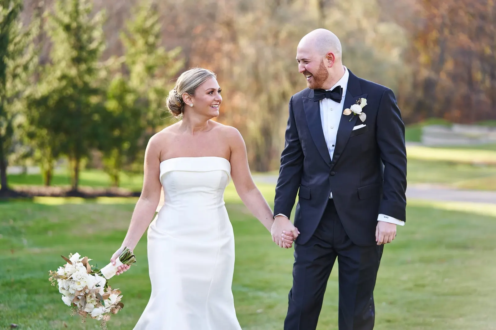 Bride and groom laughing together on the lawn in autumn light
