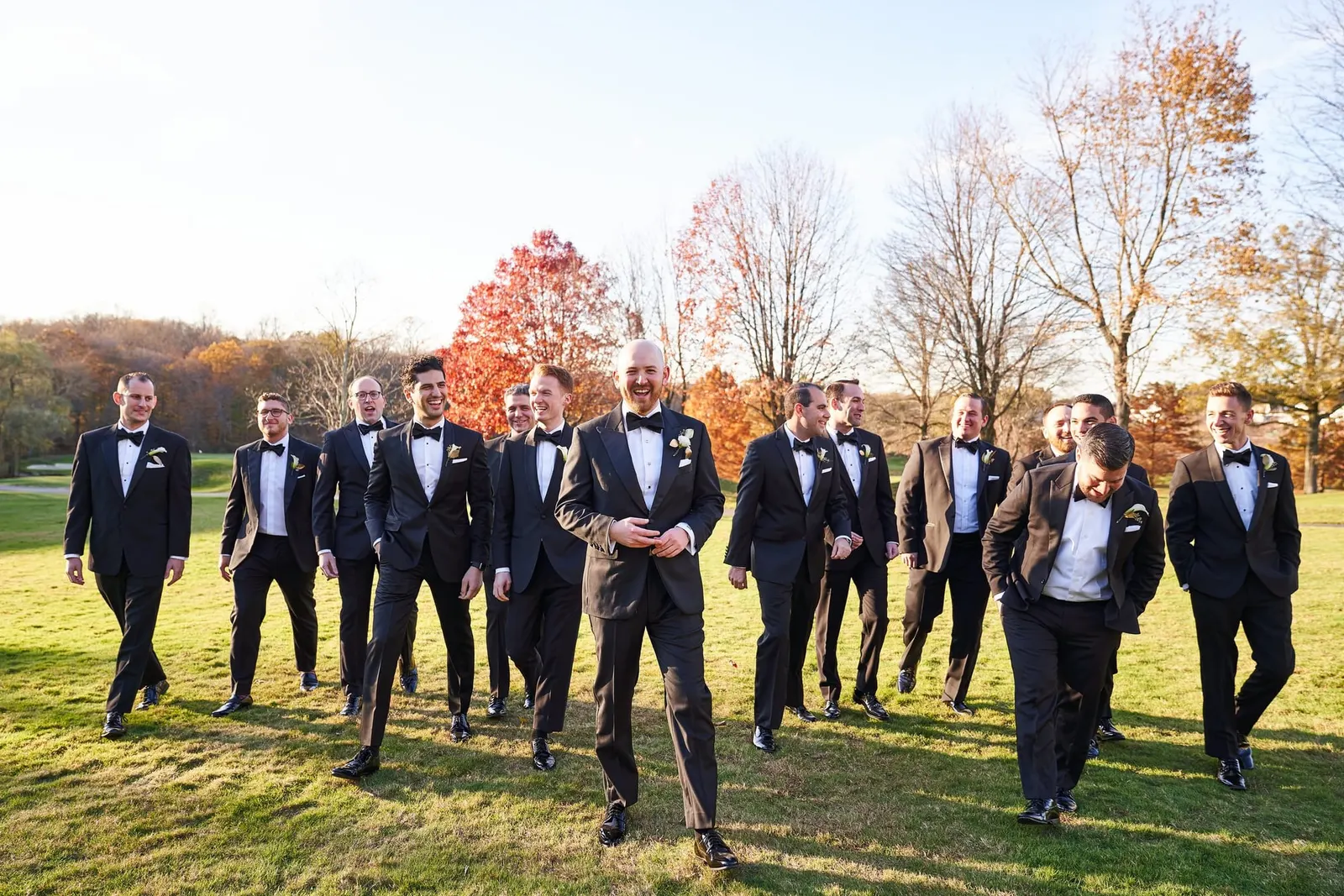 Groomsmen striding across the lawn with autumn trees behind them