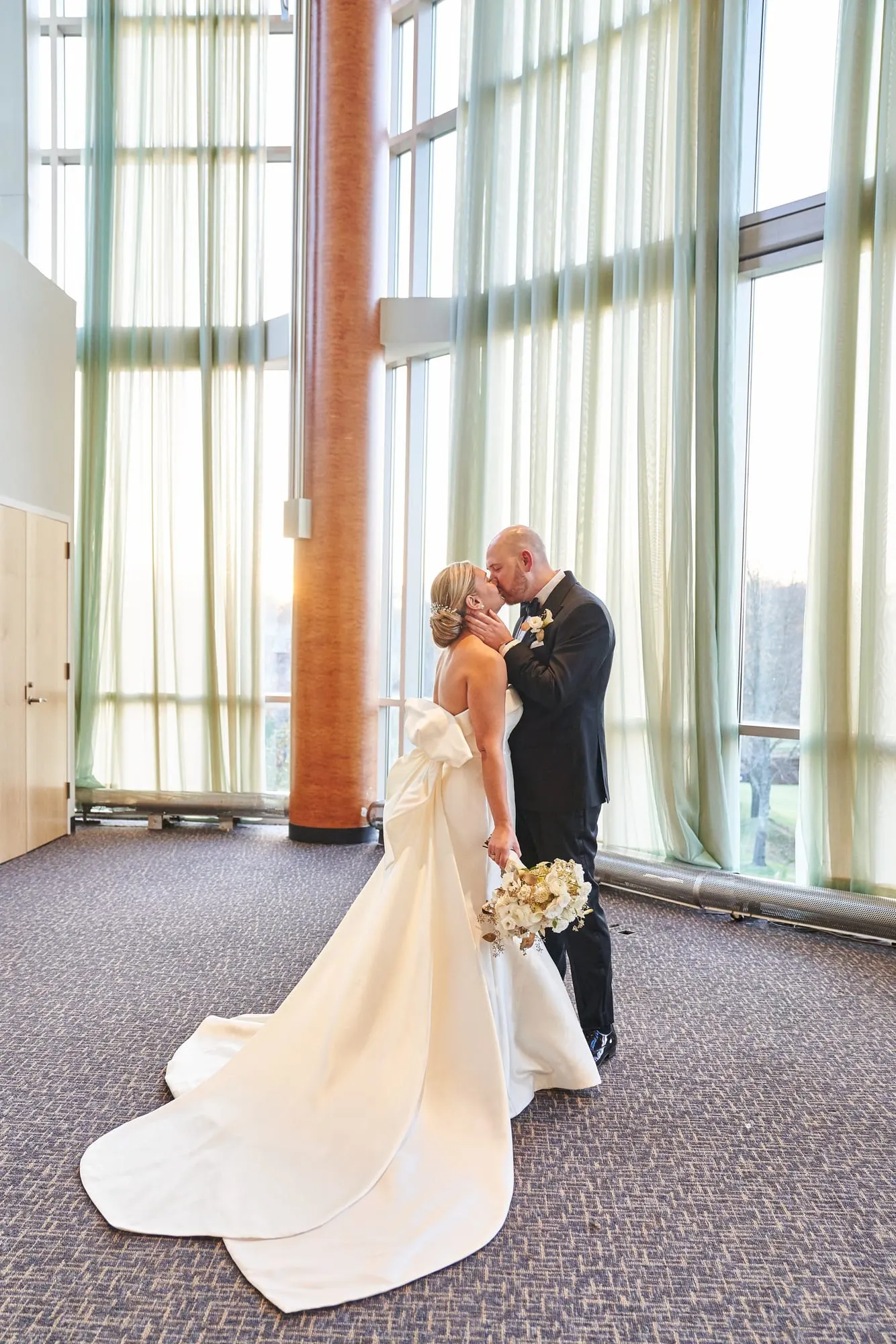 Bride and groom embracing by floor-to-ceiling windows