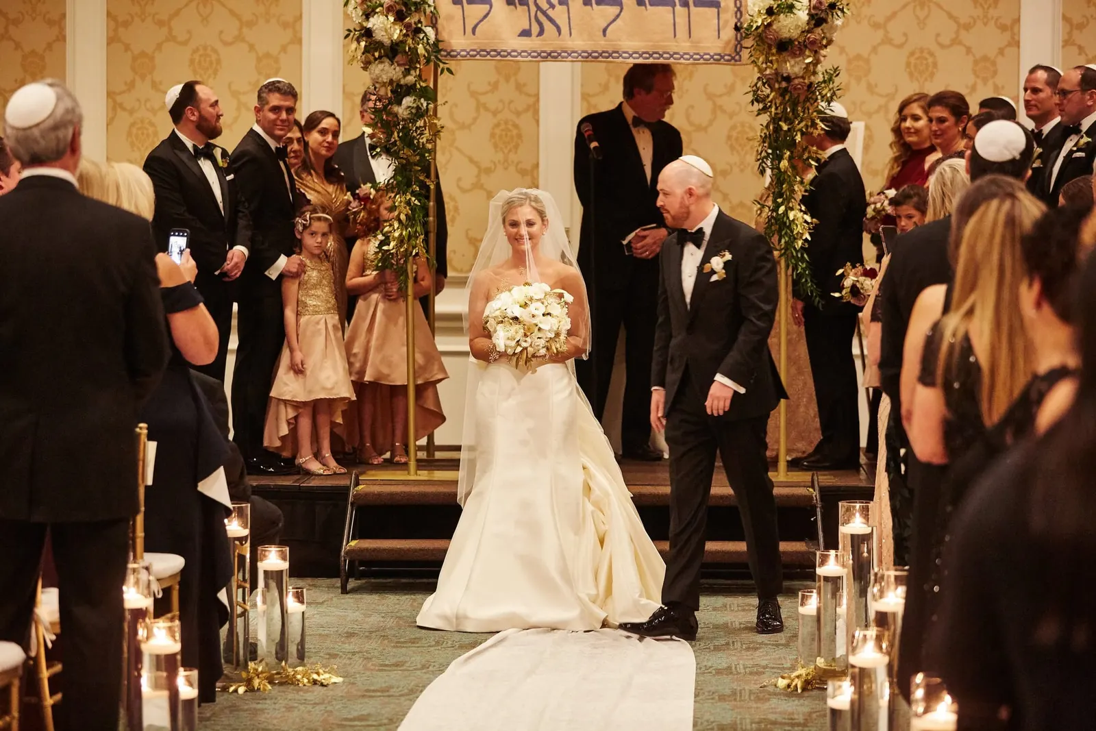 Jewish wedding ceremony under a chuppah of flowers and candlelight