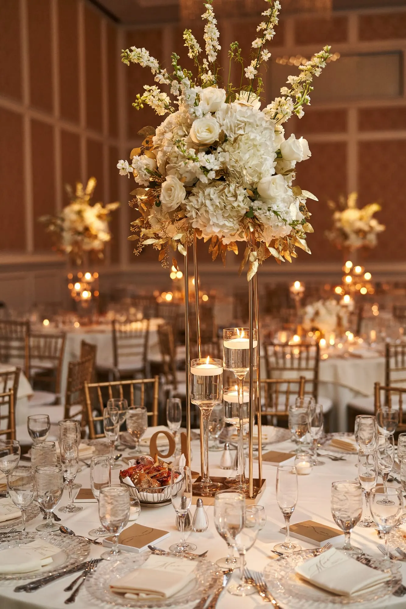 Tall centerpiece of white and blush flowers over a candlelit table