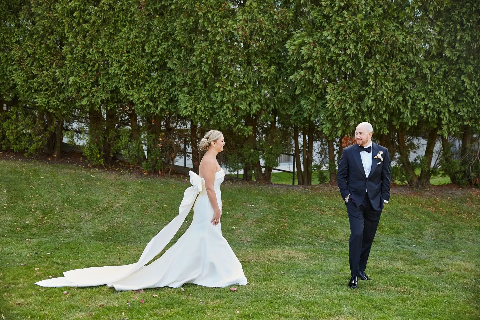 Bride and groom walking across the lawn beside a tall hedge