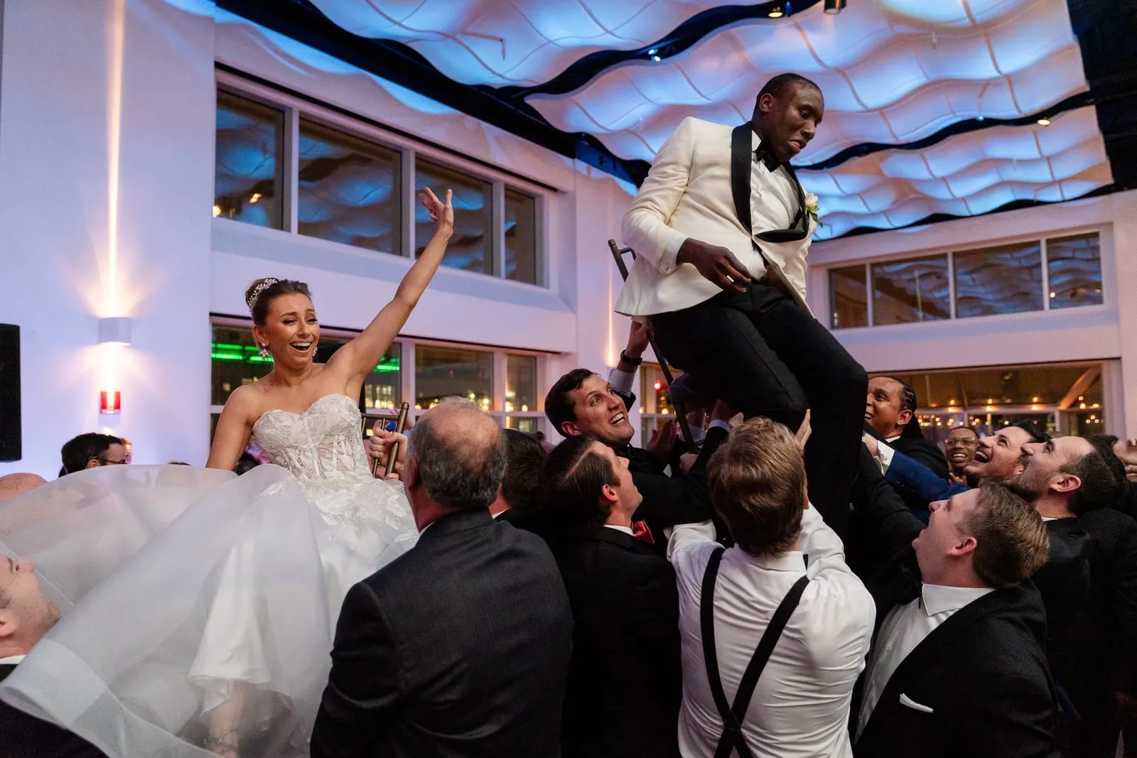 Guests lifting the bride and groom up on chairs during the reception at the Lighthouse at Chelsea Piers